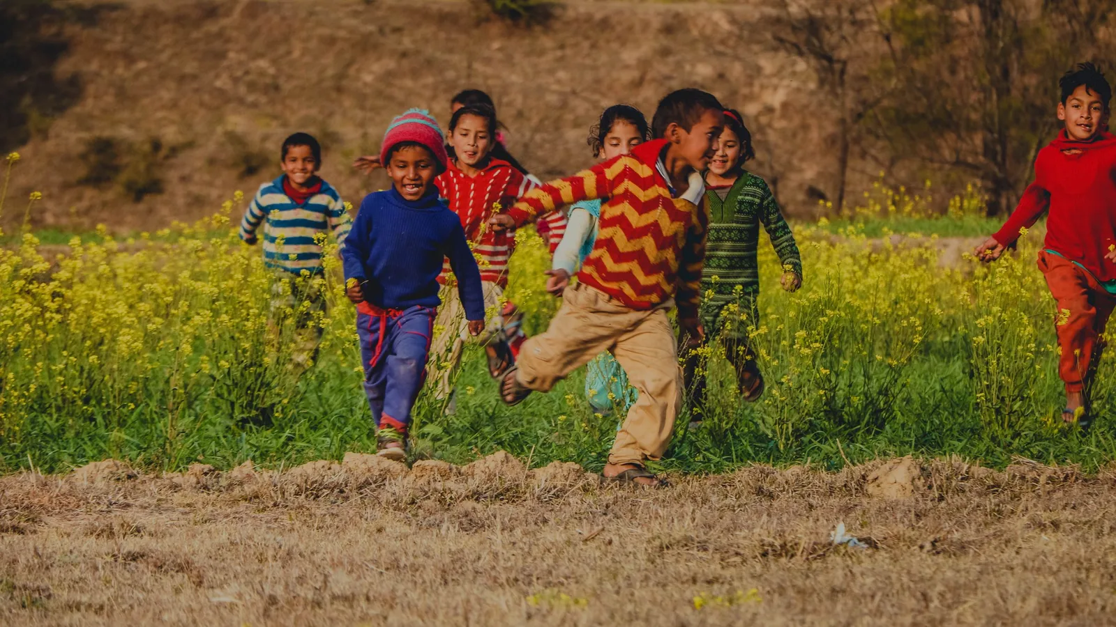 A group of laughing children running through a field of yellow flowers