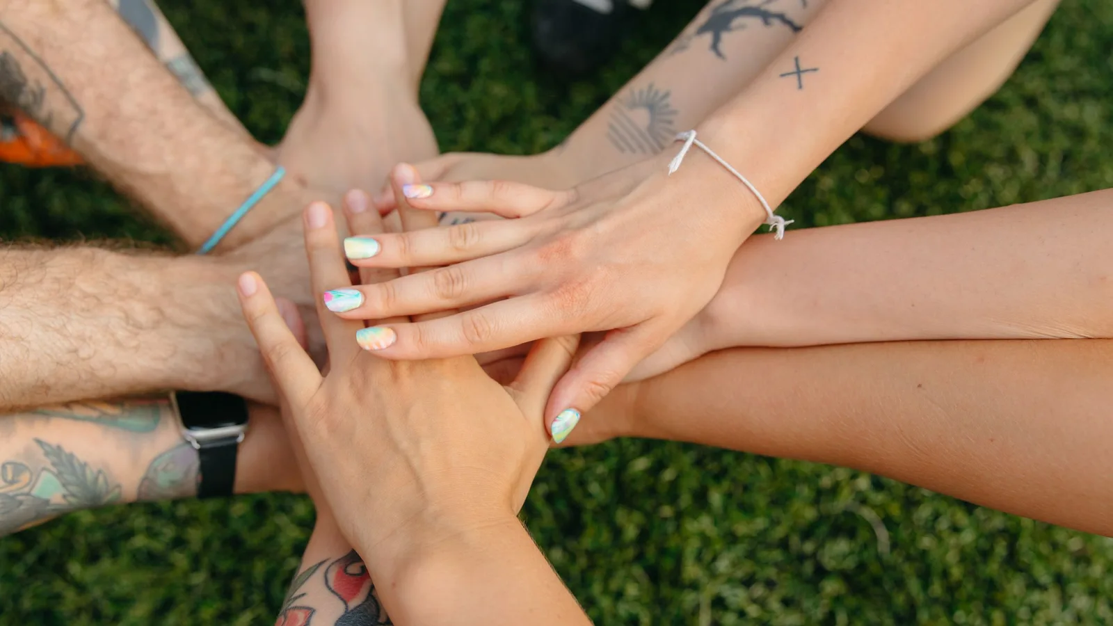 Many hands stacked together over green grass