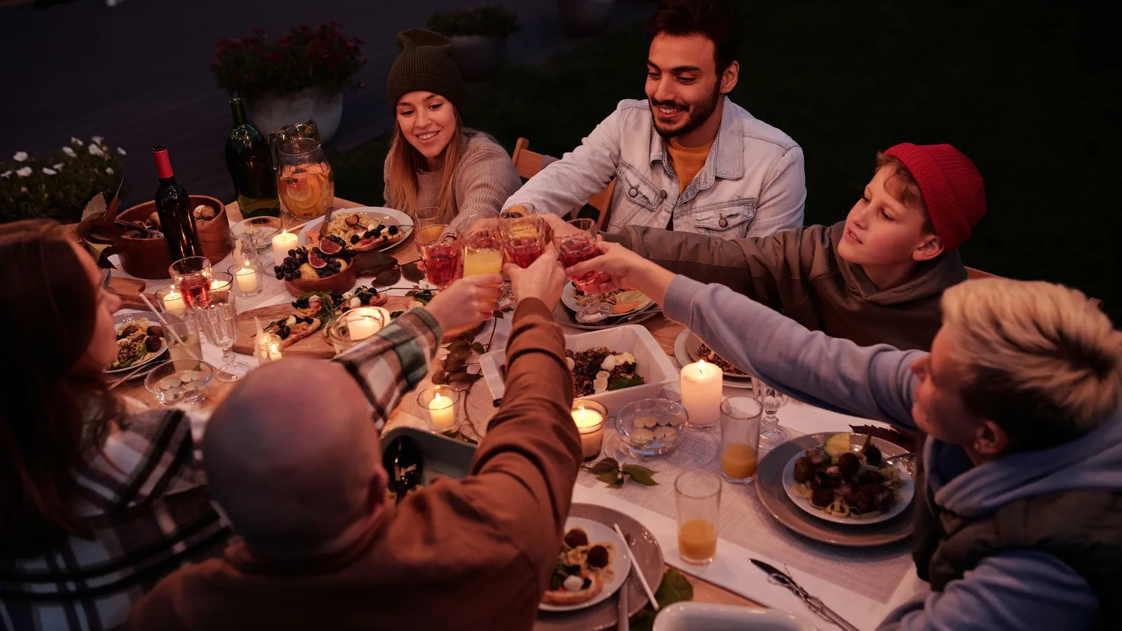 Friends raising glasses at a long outdoor dinner table lit by candles