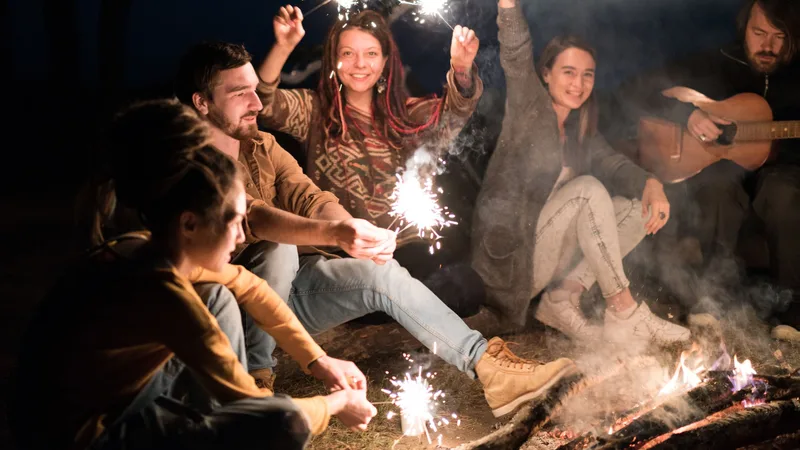 Friends around a campfire at night holding sparklers while one plays guitar