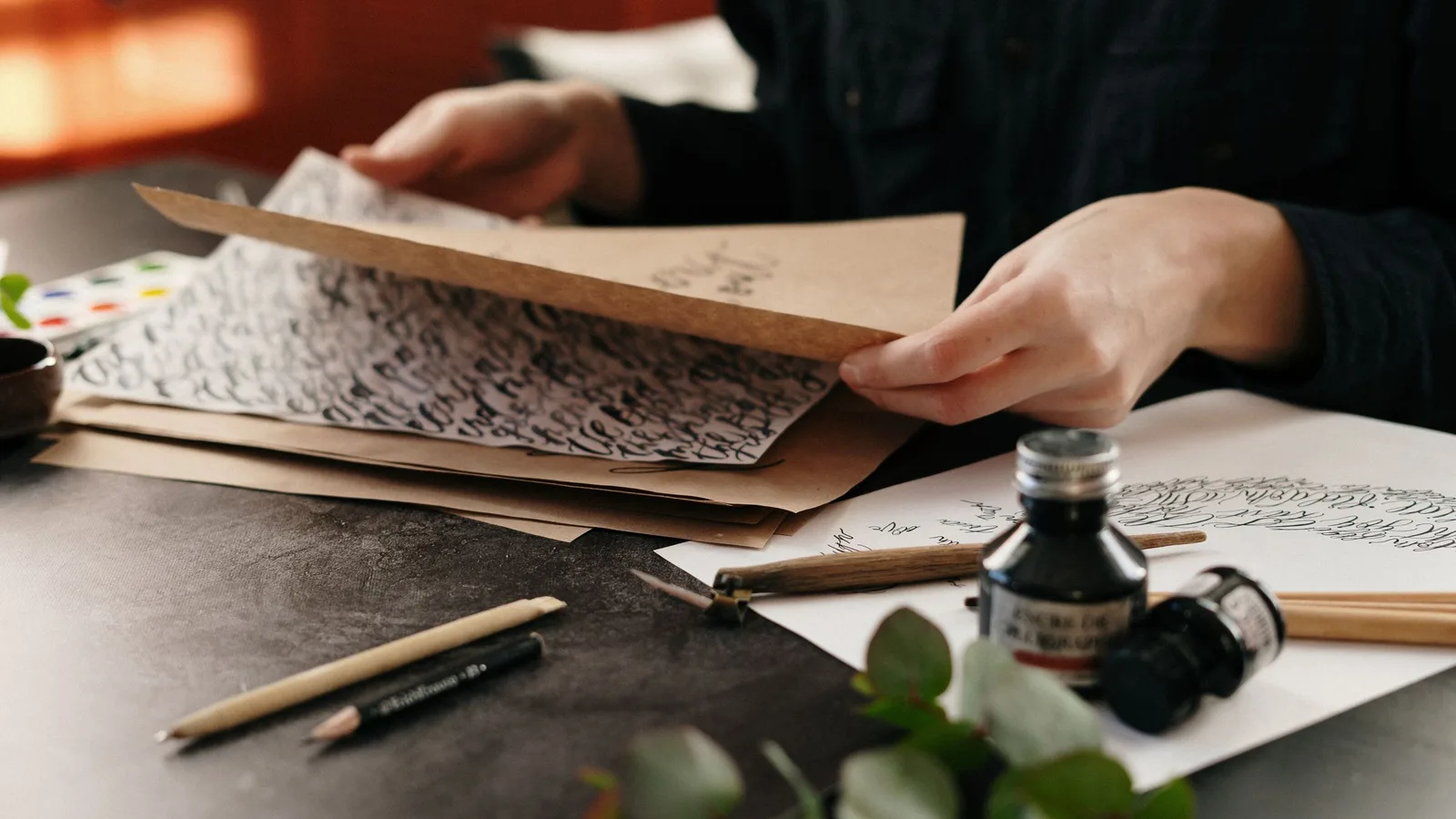 Hands sorting handwritten letters beside a bottle of ink