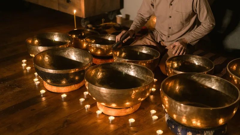 A practitioner playing a set of singing bowls surrounded by candlelight