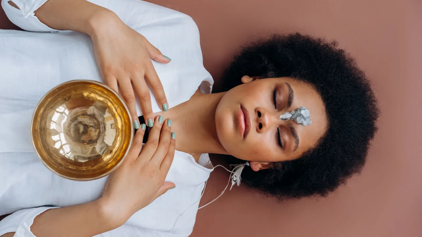 A woman lying with her eyes closed and a singing bowl resting on her chest