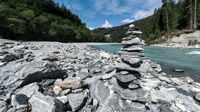 A cairn of stacked stones on a riverbank below forested mountains