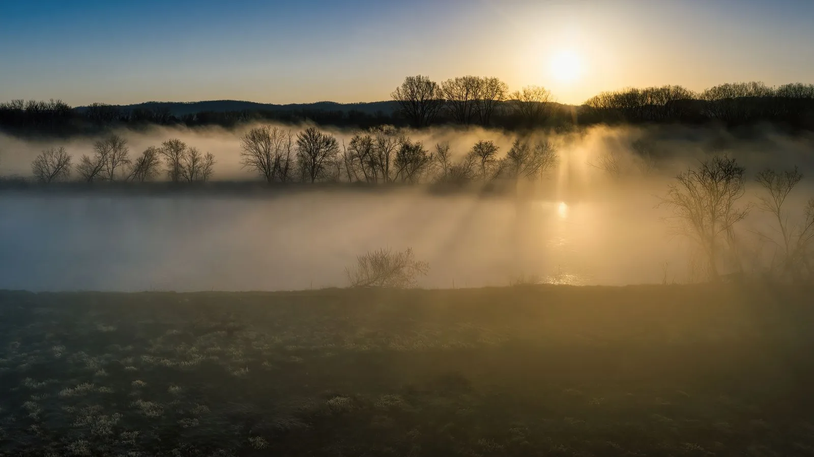 Sunrise over a misty lake with light breaking through the trees