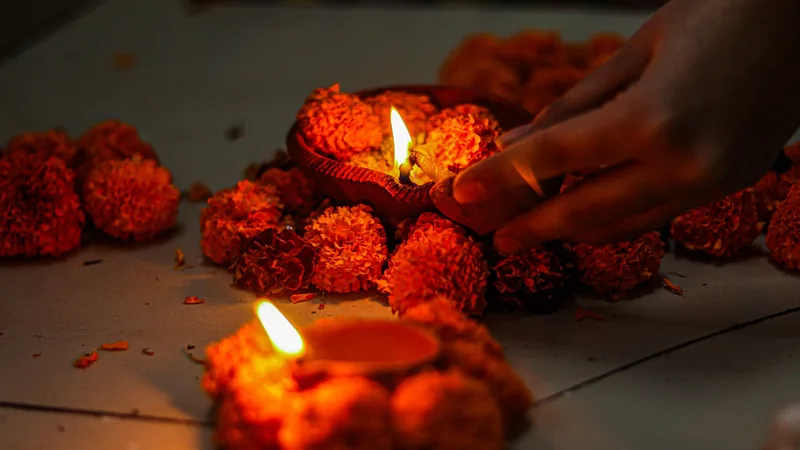 A hand lighting a small oil lamp among orange marigold flowers