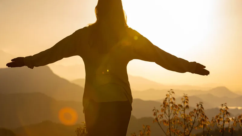 Silhouette of a woman with open arms facing the sunrise over misty hills